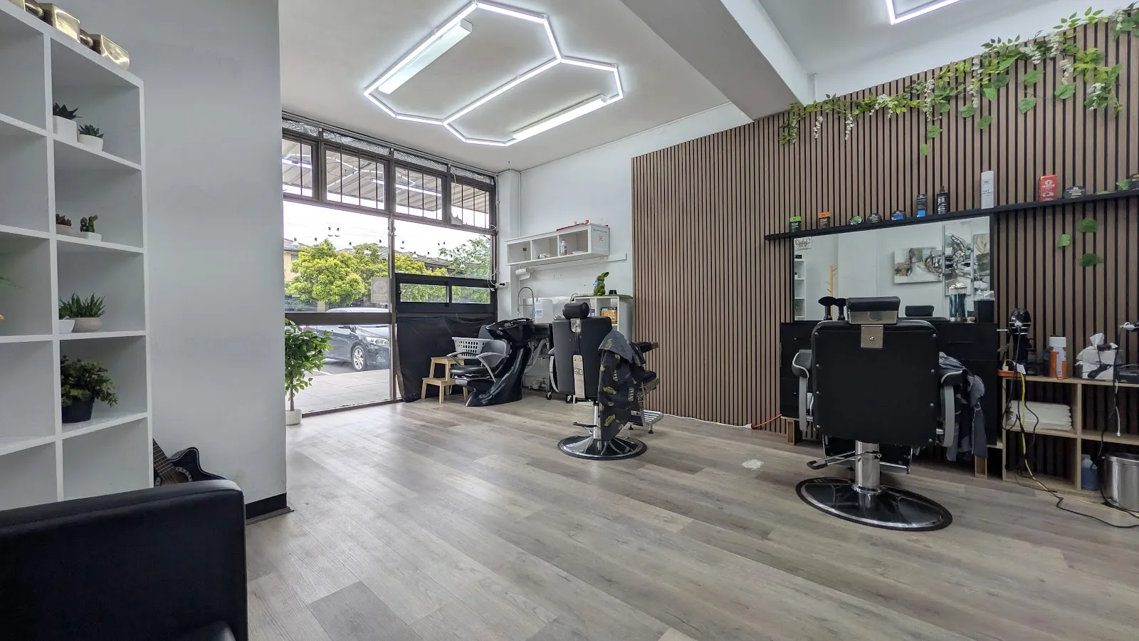 Inside Old City Barbers: two black barber chairs, a timber slat wall with trailing ivy and hexagonal LED lights